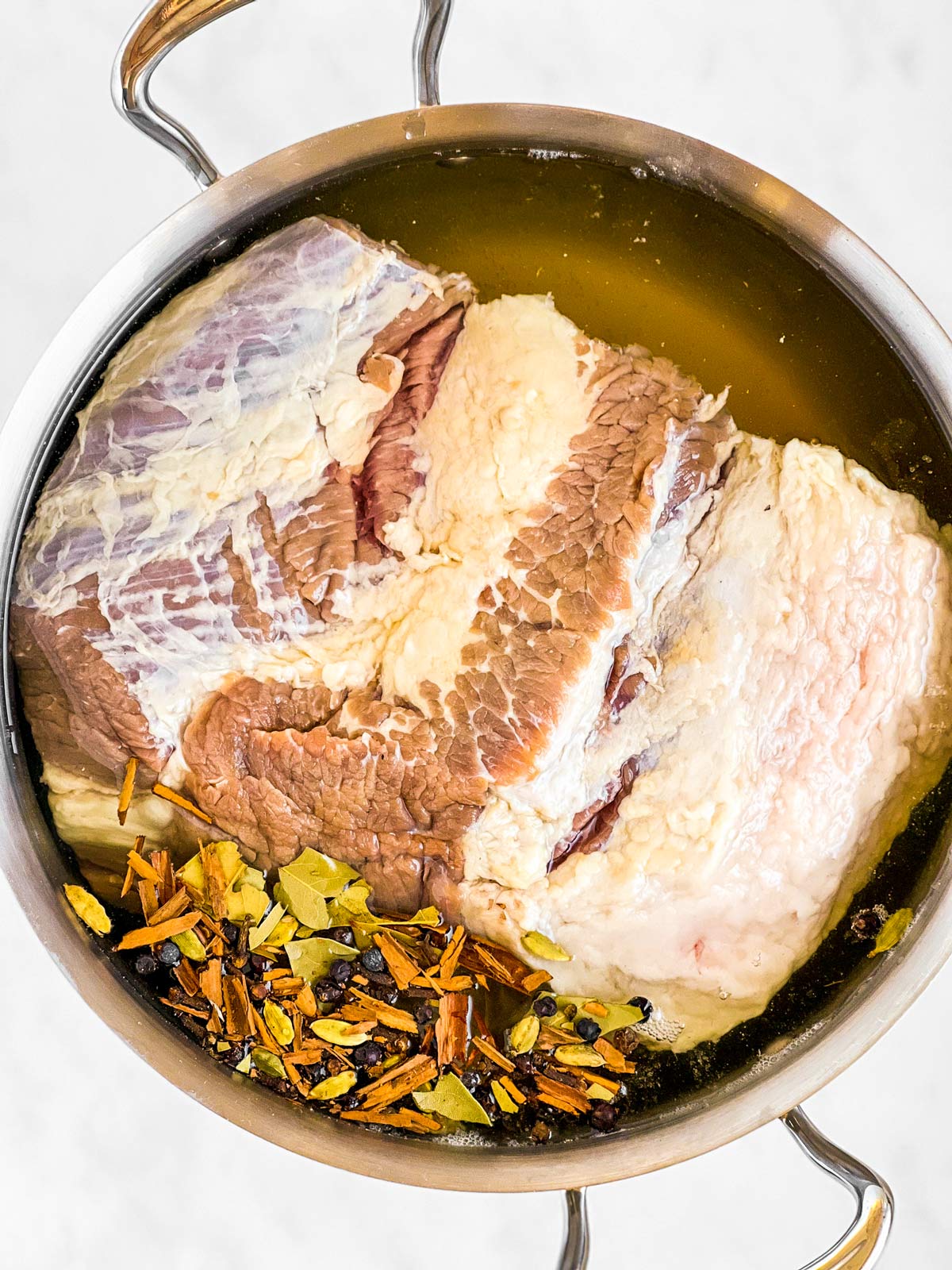 overhead view of uncooked corned beef brisket in pot with pickling spices and beer