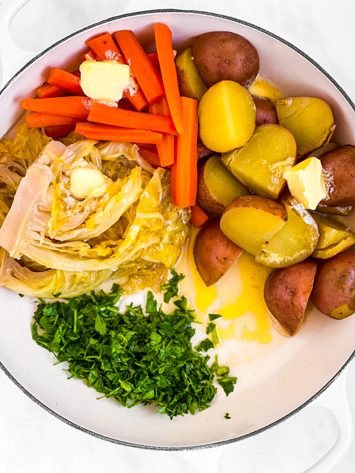 overhead view of cooked vegetables in skillet with butter and fresh parsley