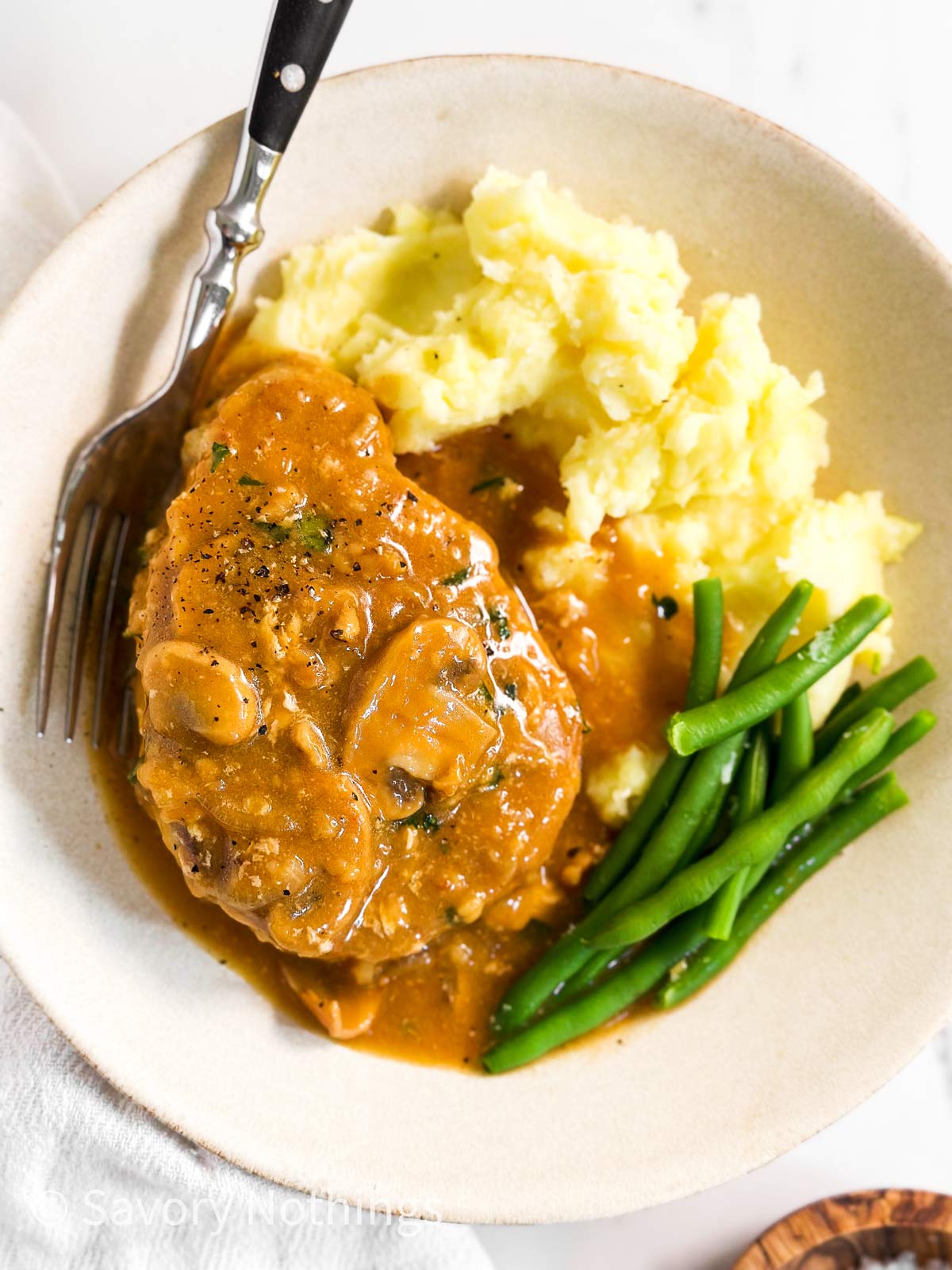 overhead view of white plate with mashed potatoes, green beans, pork chop and mushroom gravy