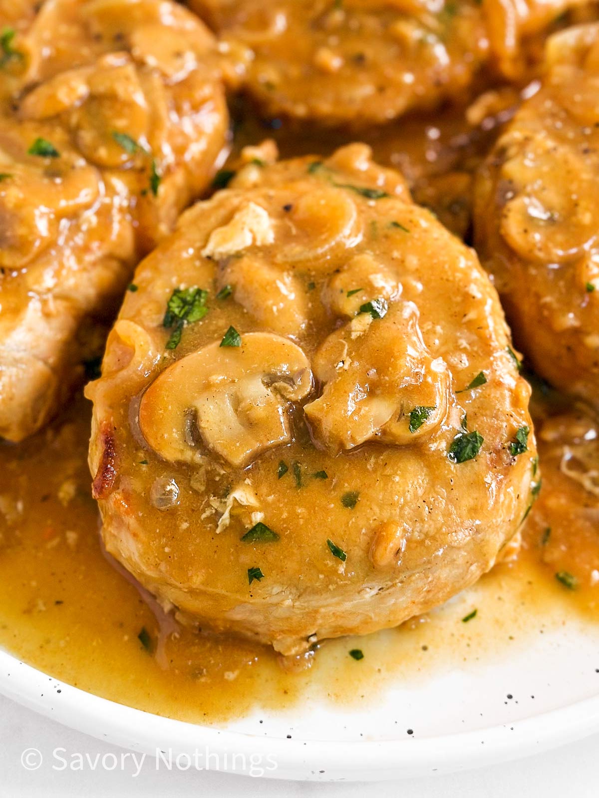 frontal close up view of pork chops on white plate covered in mushroom gravy