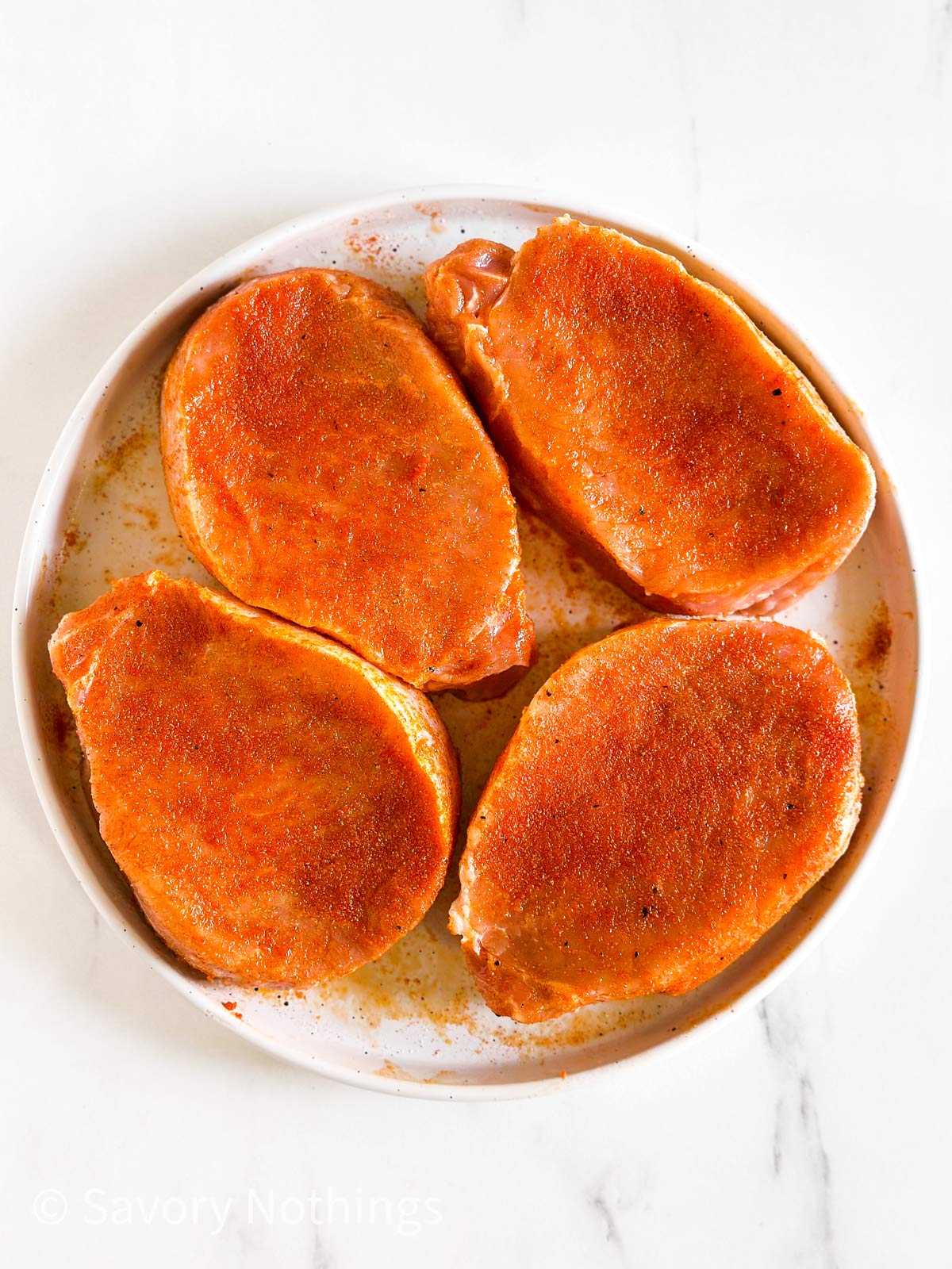 overhead view of 4 raw, seasoned pork chops on white plate