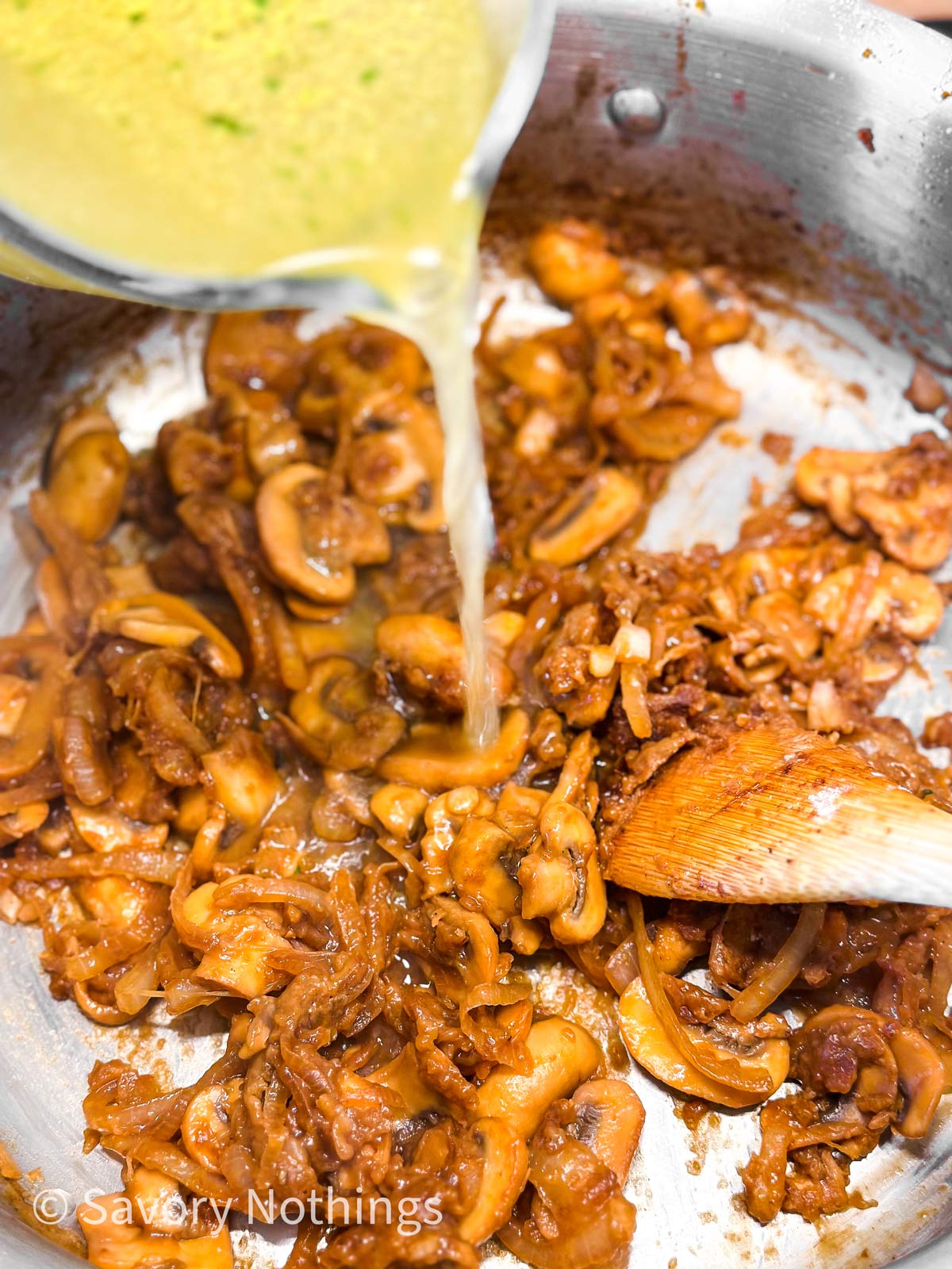 broth pouring from glass measuring jug into skillet  with cooked mushrooms and onions