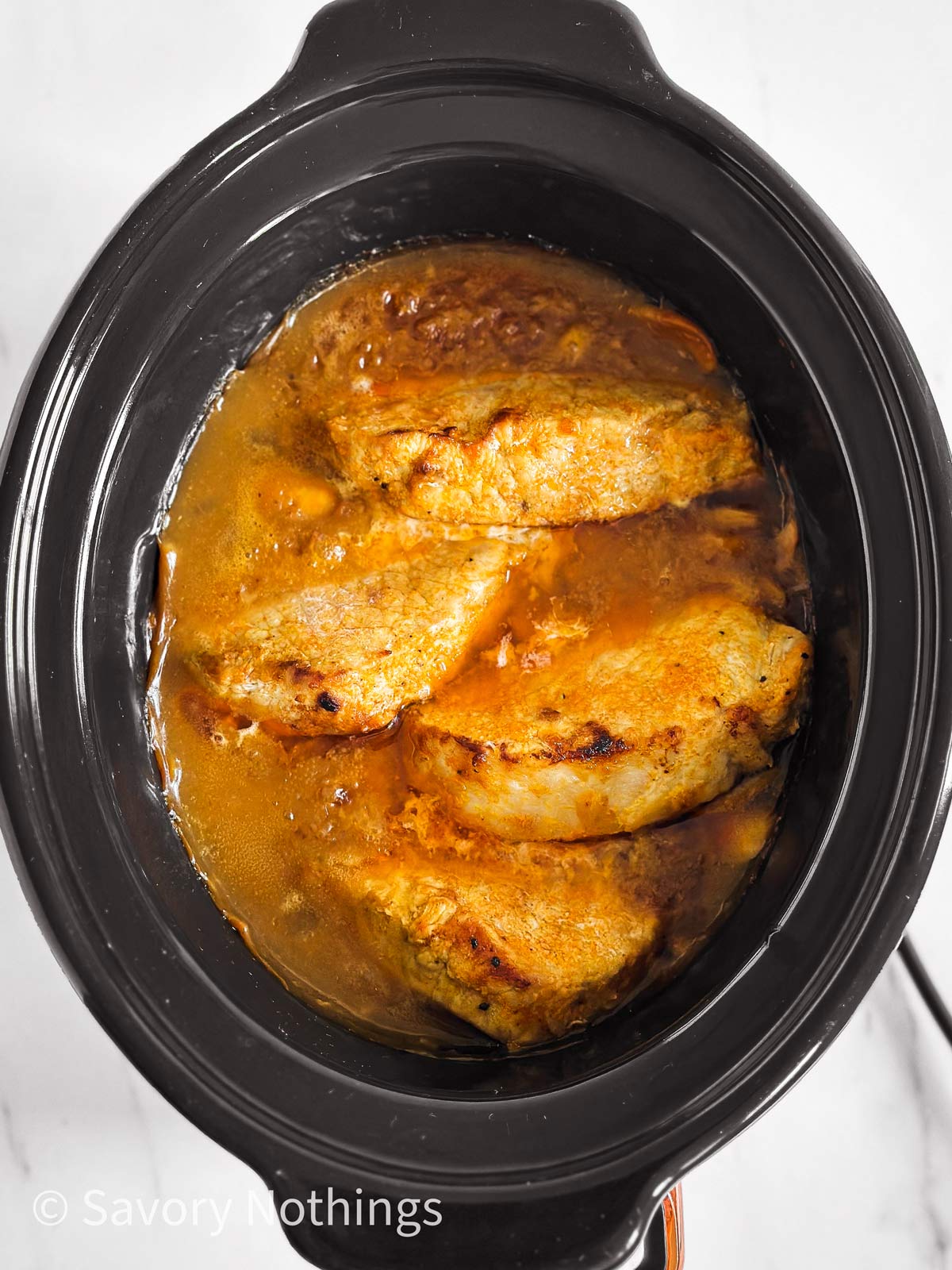 overhead view of cooked pork chops and gravy in black slow cooker crock