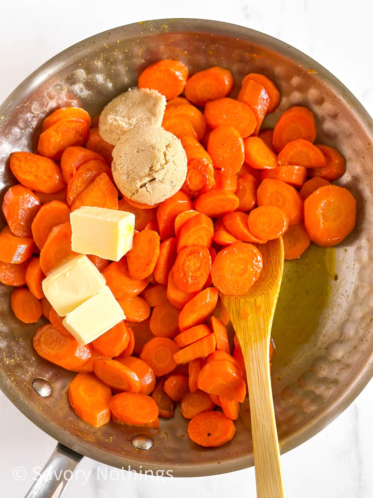 overhead view of cooked sliced carrots in skillet topped with brown sugar and butter