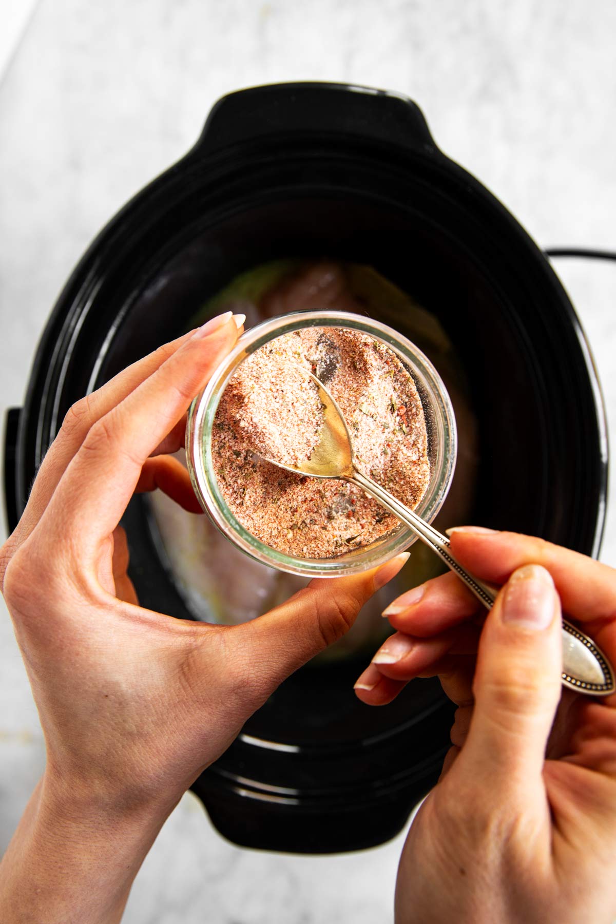 female hands mixing seasoning in small glass bowl over slow cooker