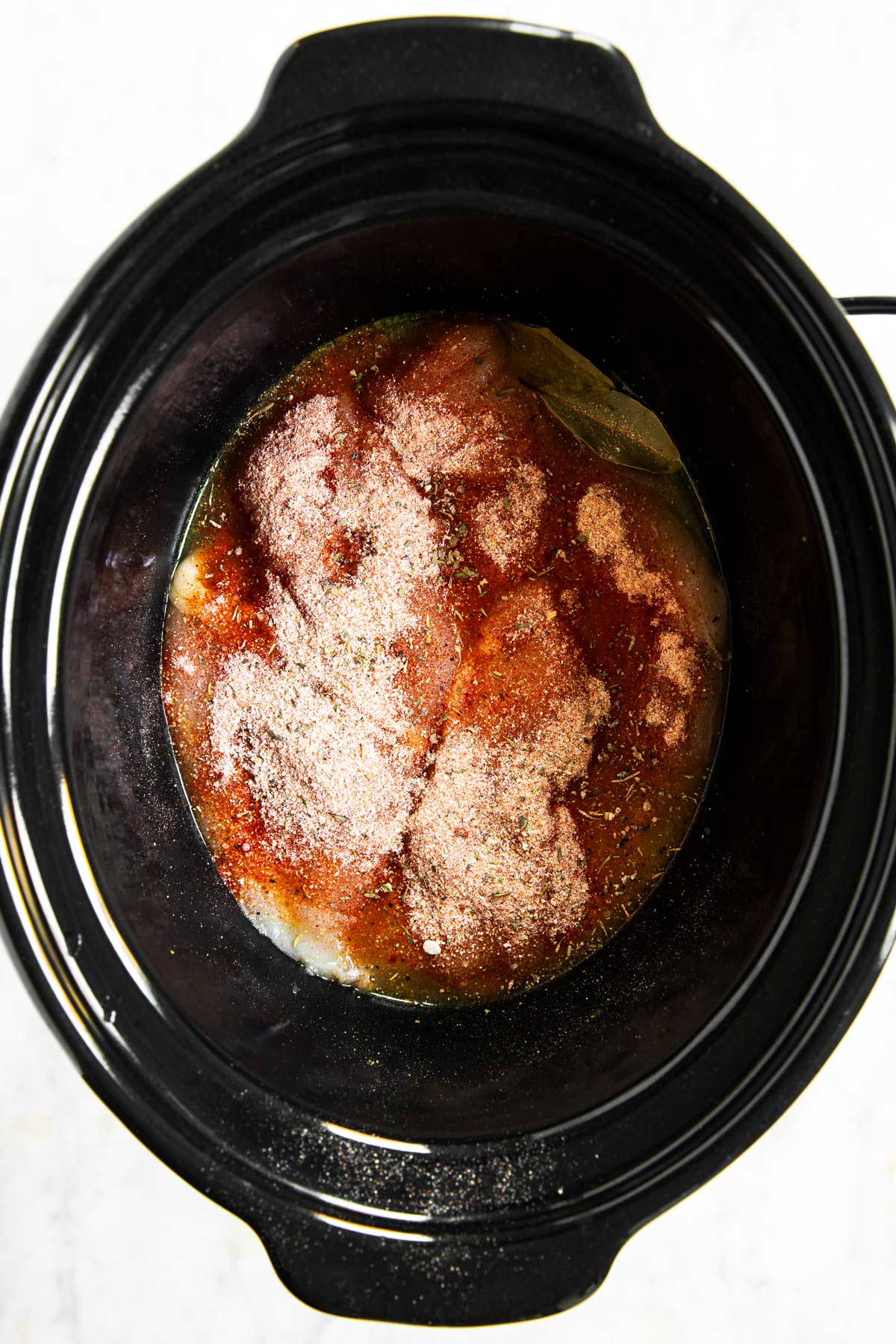 overhead view of raw chicken breast with seasoning on top in slow cooker crock