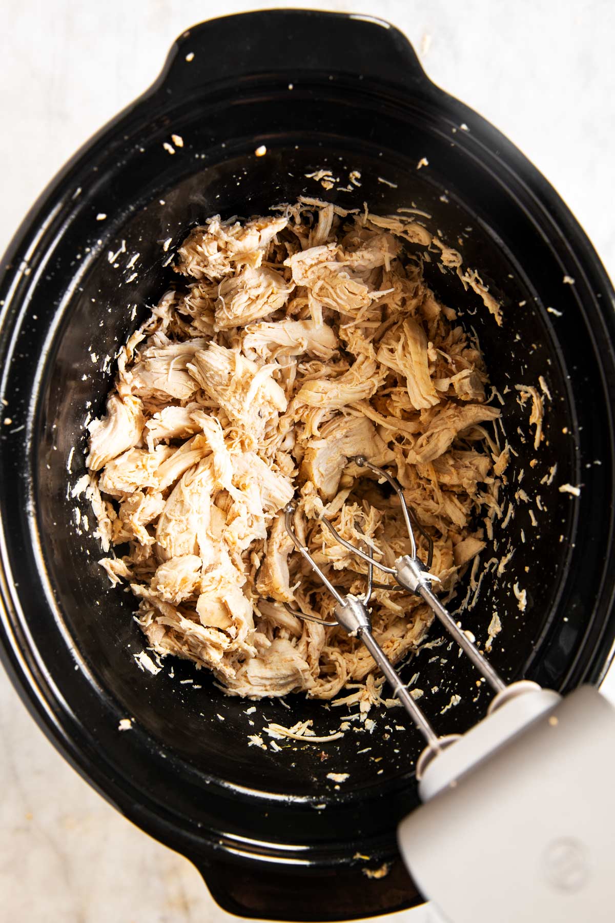 hand mixer in crock of slow cooker with shredded chicken