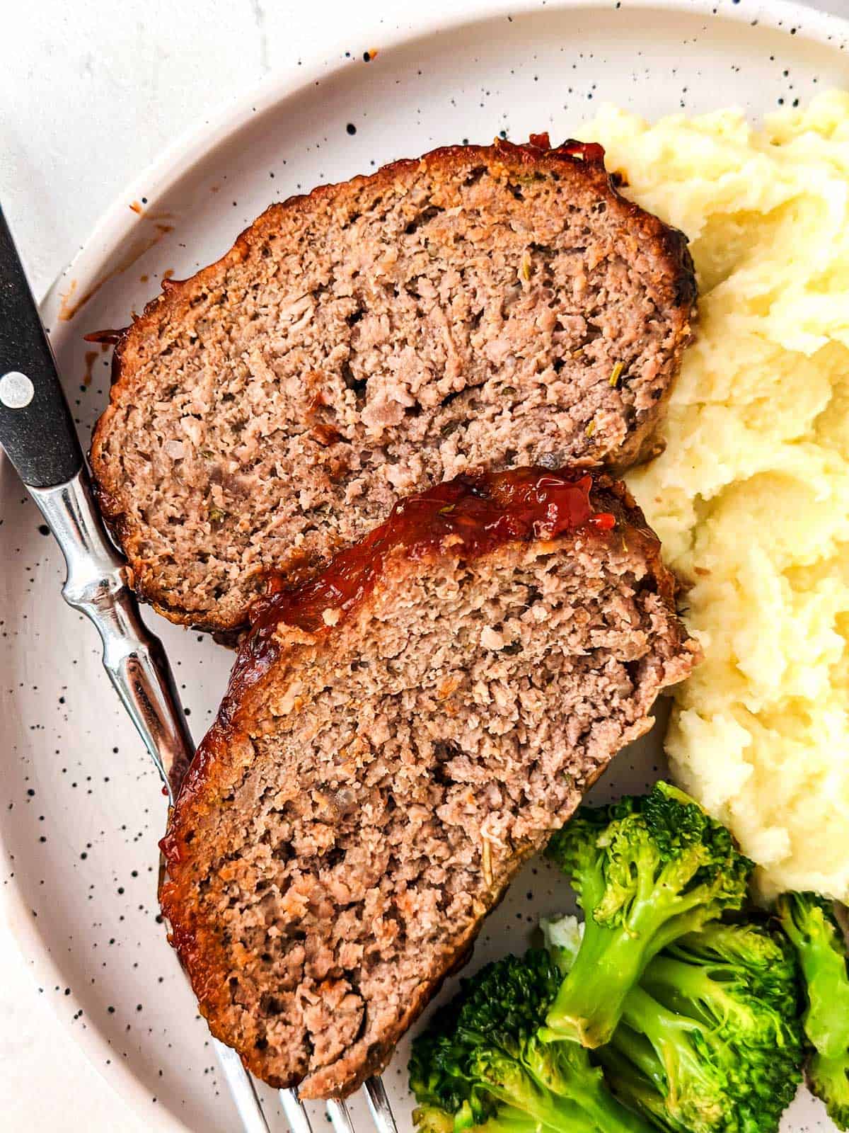 overhead view of two meatloaf slices on plate with broccoli and mashed potatoes