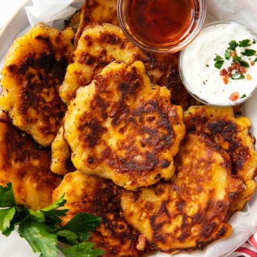 overhead view of basket filled with corn fritters with bowls of maple syrup and sour cream tucked in