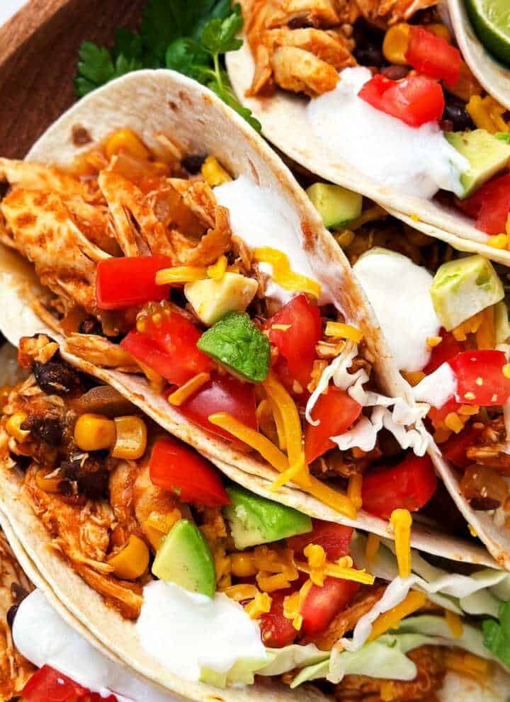 overhead close up view of crock pot chicken tacos with toppings on wooden platter