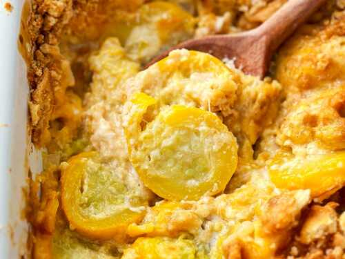 frontal close up of wooden spoon scooping squash casserole from a white baking dish