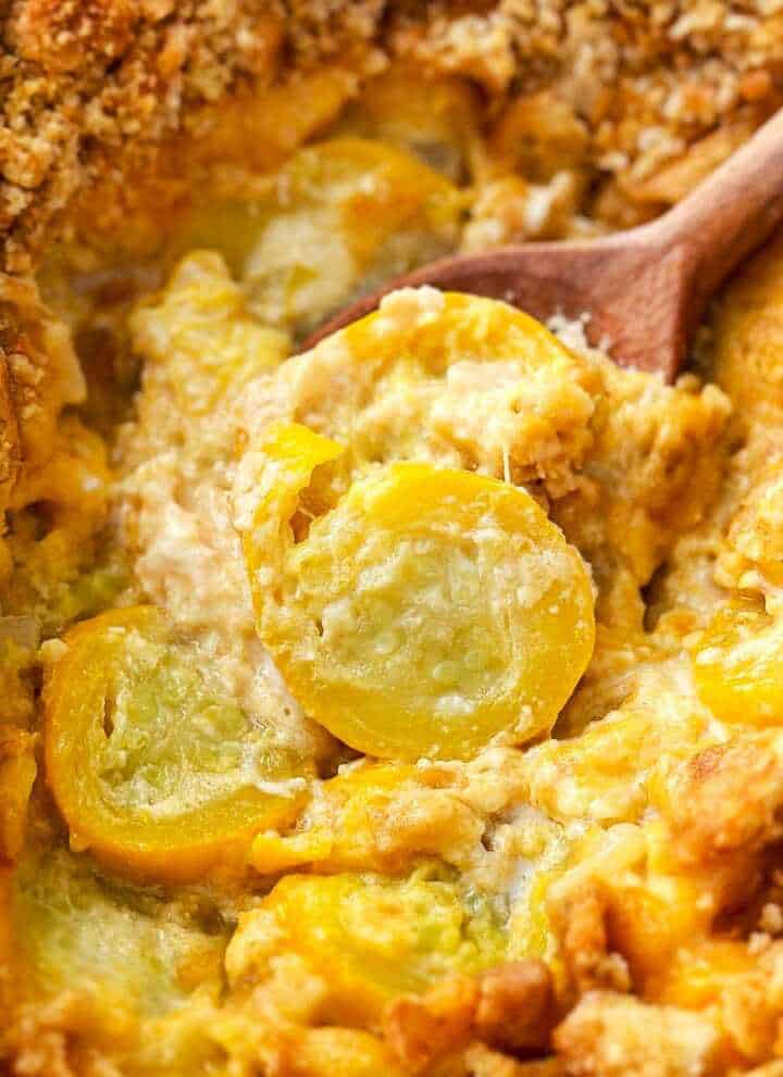 frontal close up of wooden spoon scooping squash casserole from a white baking dish