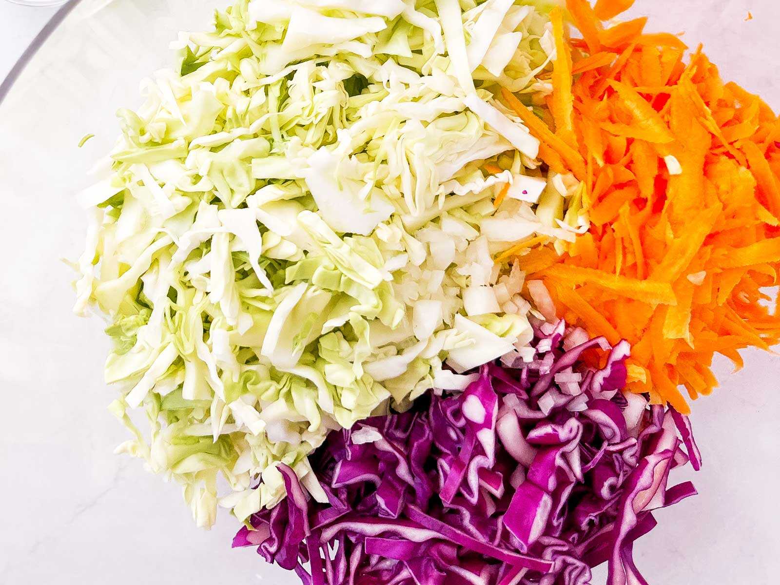 overhead view of shredded green and purple cabbage in glass bowl with shredded carrot