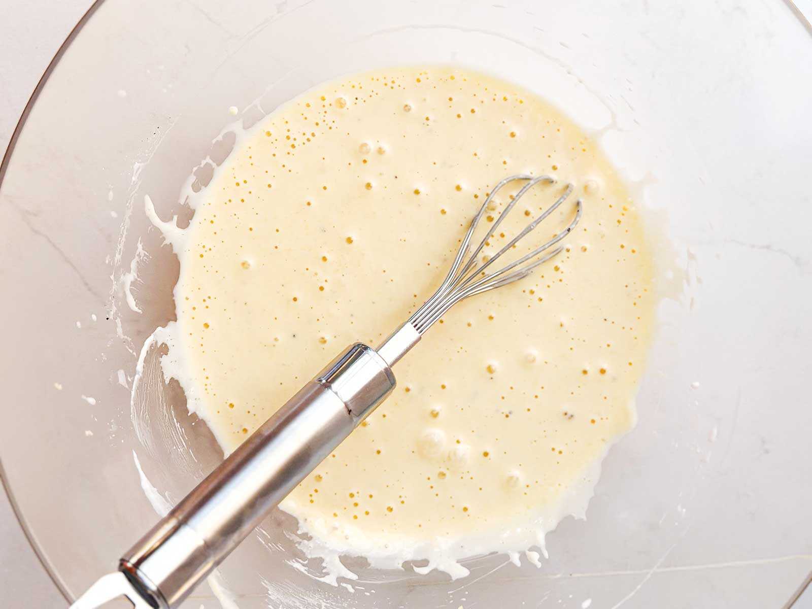 overhead view of mayonnaise dressing in glass bowl with whisk