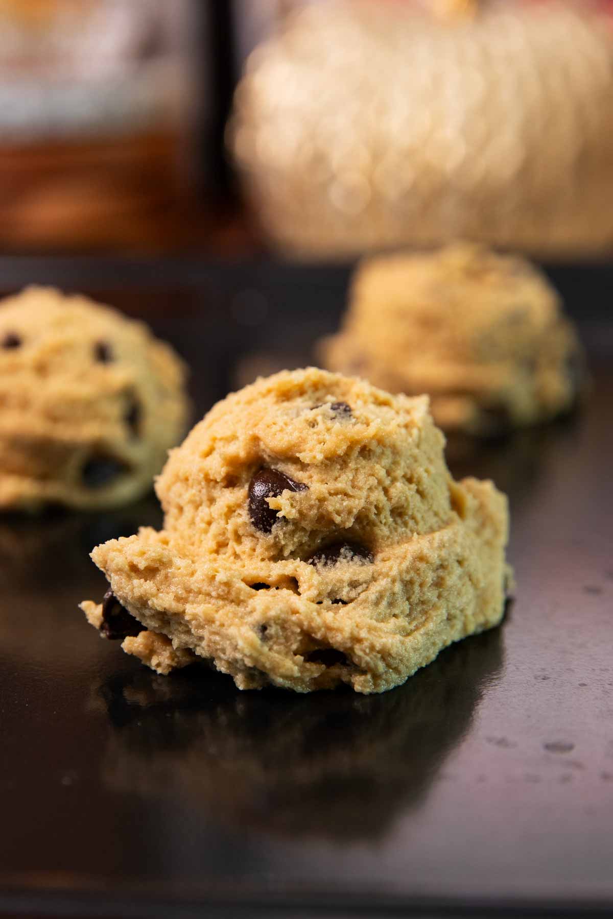 Unbaked chocolate chip cookie dough ball on a black cookie sheet.