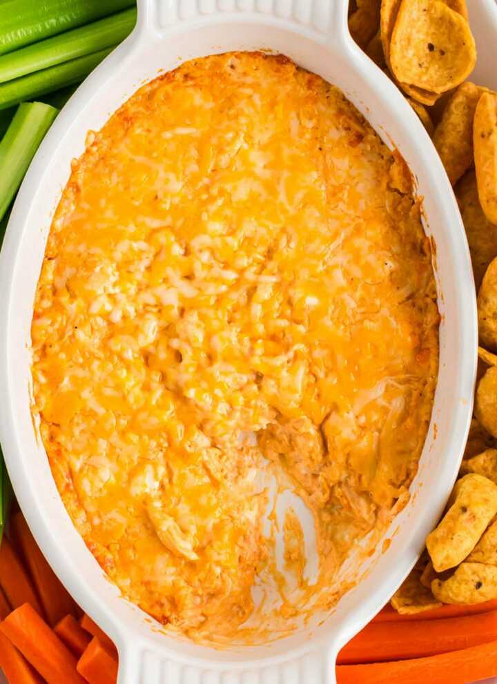 overhead view of buffalo chicken dip in white dish surrounded by chips and vegetables