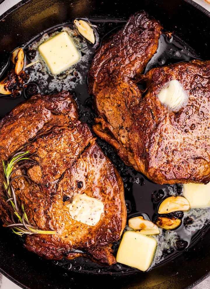 overhead view of seared steaks in cast iron skillet with butter, garlic and herbs