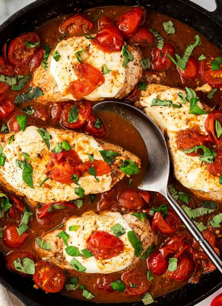 Overhead view of Caprese chicken skillet with golden seared chicken breasts, melted mozzarella, cherry tomatoes, and fresh basil in a balsamic glaze