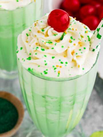 45° view of shamrock shake in tall glass decorated with whipped cream. maraschino cherry and sprinkles