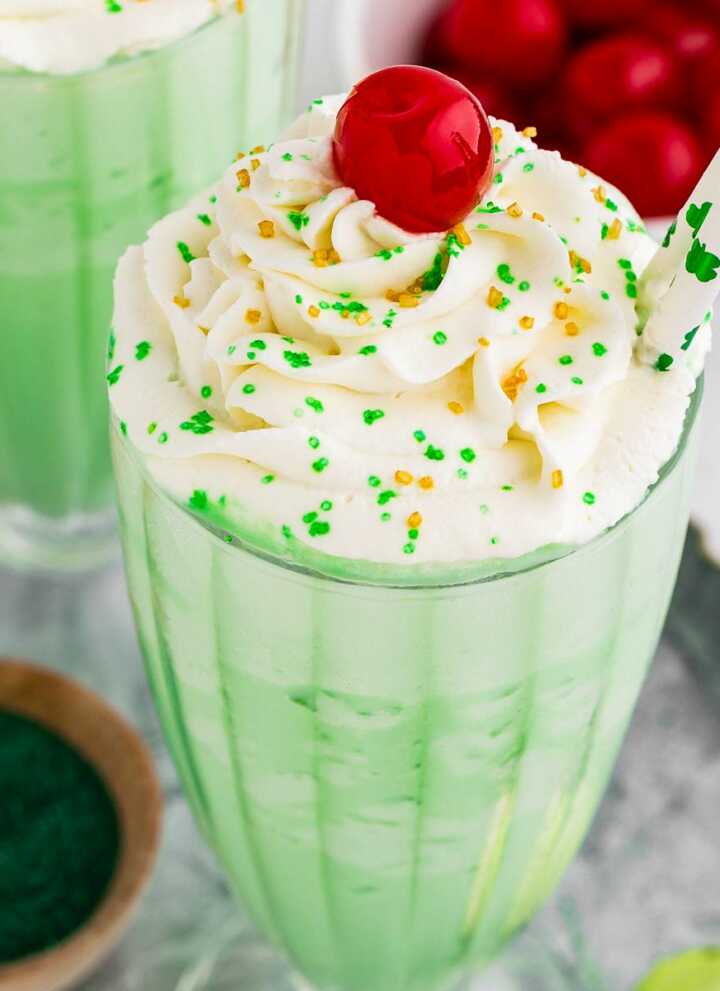 45° view of shamrock shake in tall glass decorated with whipped cream. maraschino cherry and sprinkles