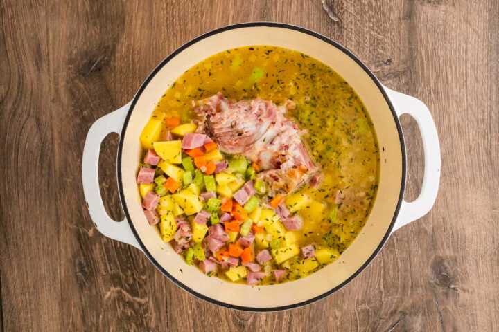 overhead view of vegetables and ham in broth in Dutch oven