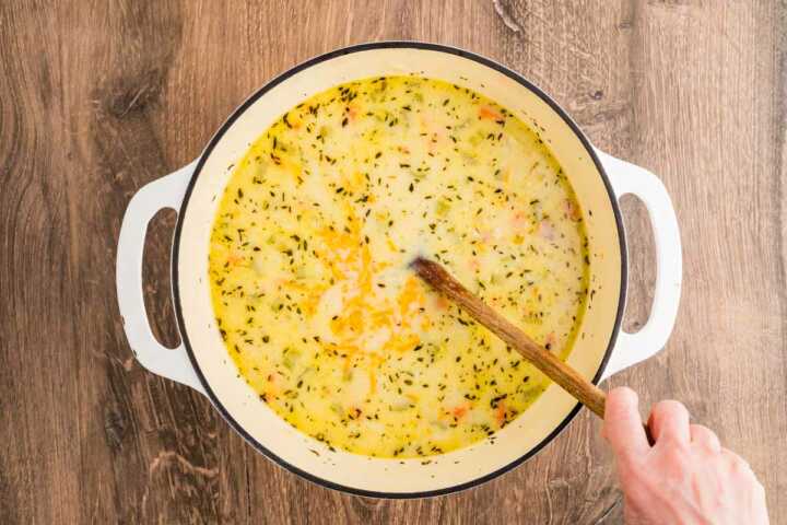 female hand stirring ham and potato soup in Dutch oven