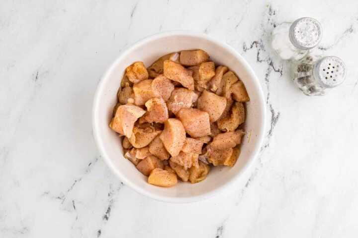 overhead view of diced chicken breast with seasoning in bowl