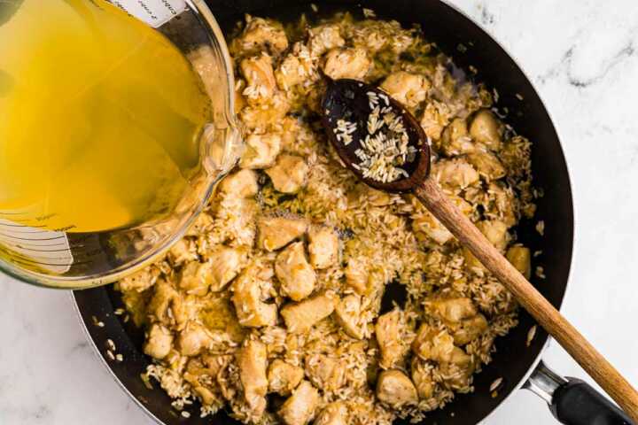 broth pouring into skillet with chicken and rice