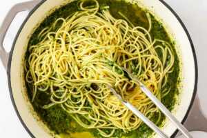 overhead view of pesto and pasta being tossed together in a skillet