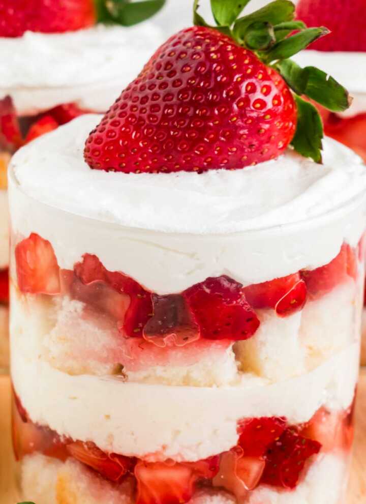 Frontal view of individual strawberry shortcake trifles layered in glass jars with whipped cream and fresh strawberry garnish