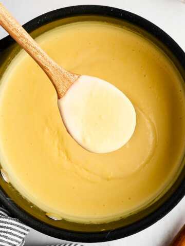 overhead view of saucepan filled with vanilla sauce with wooden spoon scooping some out