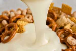 melted white candy melts pouring over Chex mix ingredients