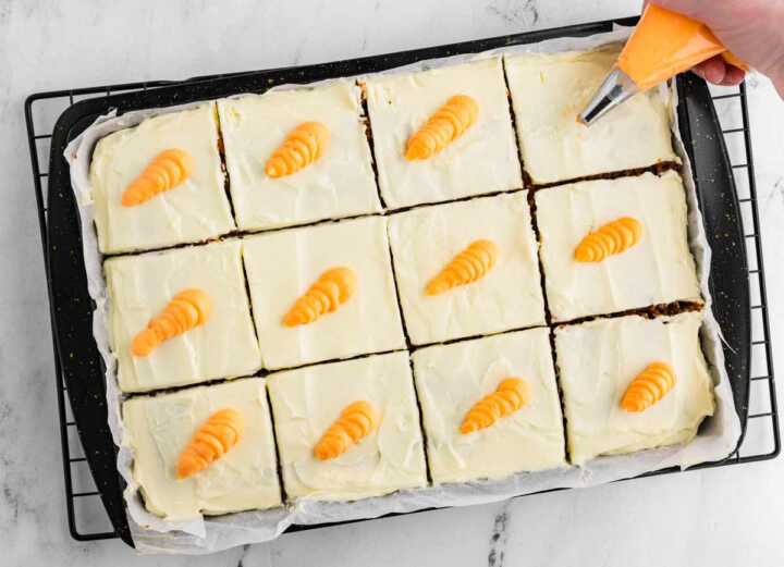 overhead view of piping bag adding frosting carrots to carrot sheet cake