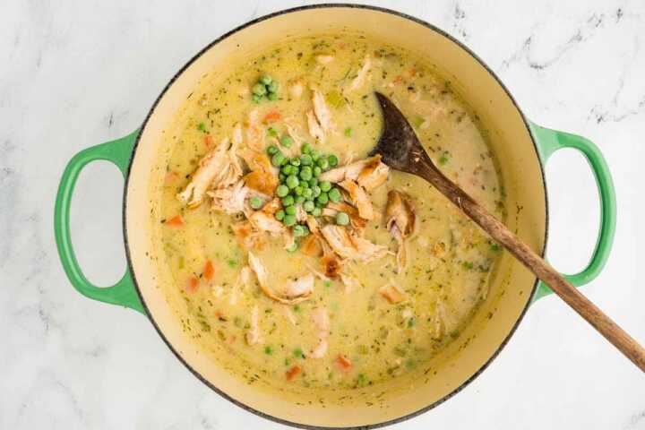overhead view of shredded chicken and frozen peas in chicken stew