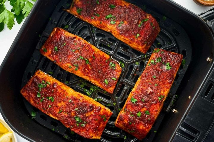 overhead view of four air fried salmon fillets in air fryer basket