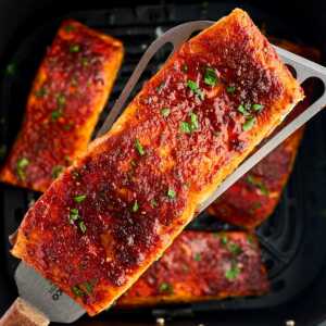 overhead close up view of cooked salmon filled being held over air fryer basket