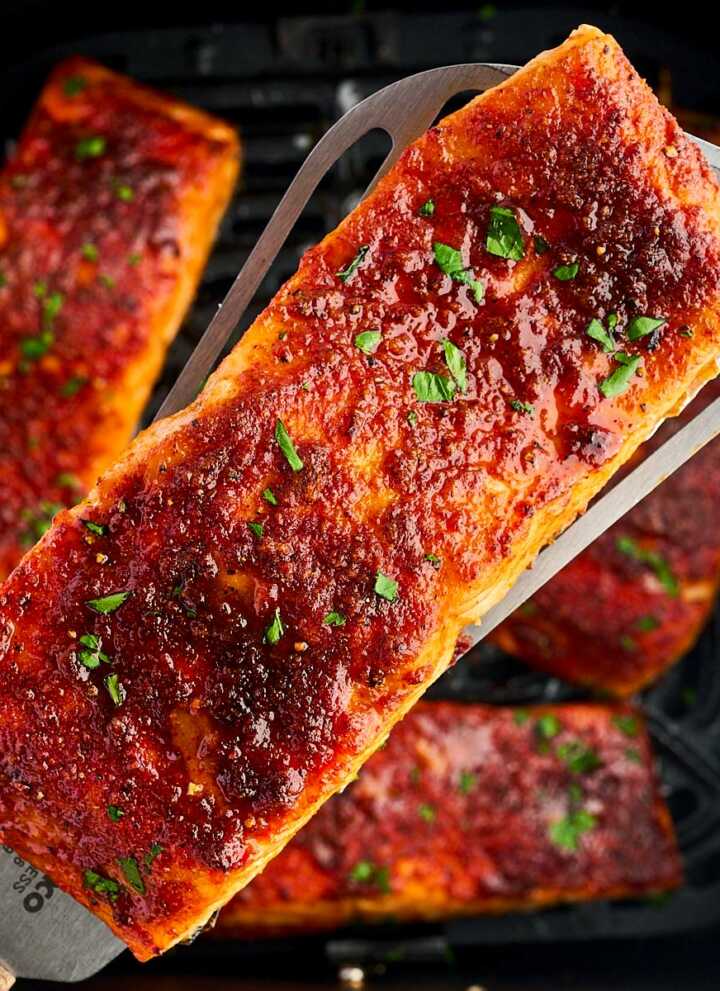 overhead close up view of cooked salmon filled being held over air fryer basket