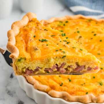 frontal view of slice of ham and cheese quiche being lifted from the pie dish