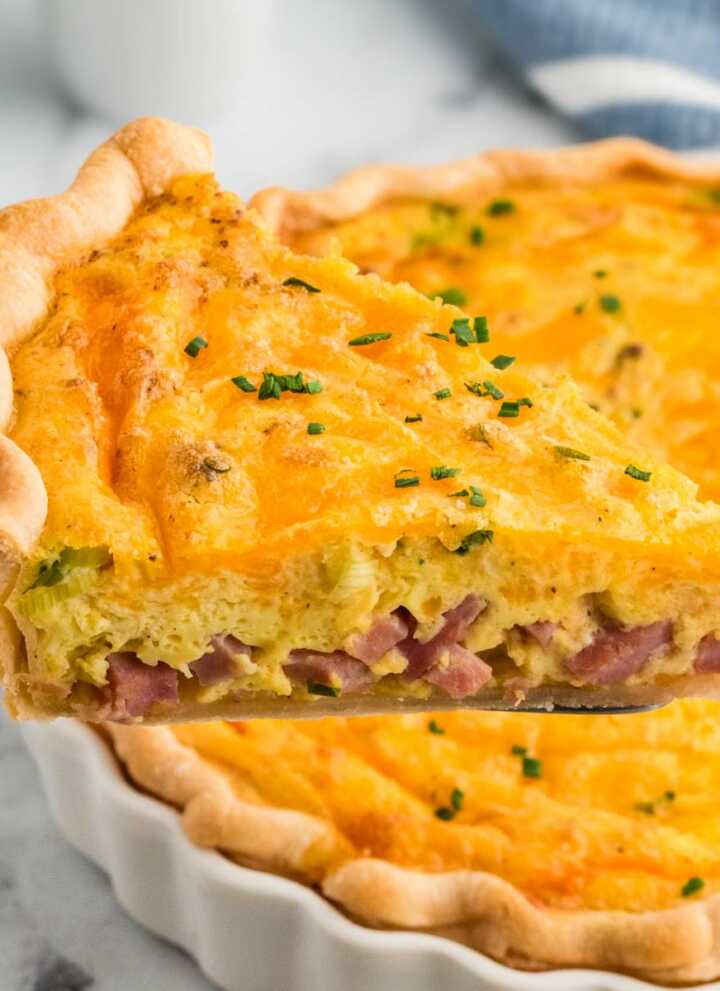 frontal view of slice of ham and cheese quiche being lifted from the pie dish