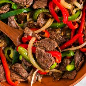 overhead view of steak with peppers and onions with wooden spoon