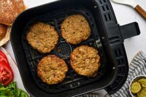 turkey burgers in air fryer basket with burger fixings around the basket