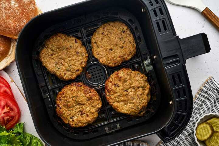 turkey burgers in air fryer basket with burger fixings around the basket