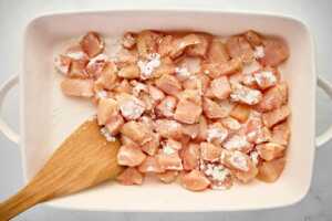 raw diced chicken being tossed with cornstarch and seasoning
