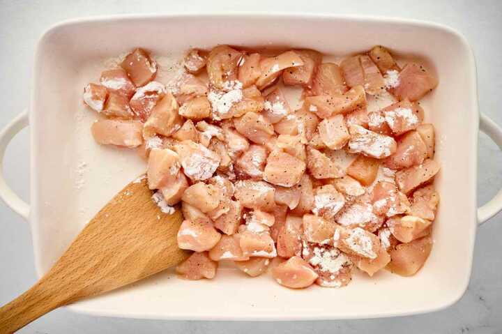 raw diced chicken being tossed with cornstarch and seasoning