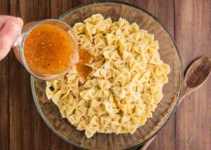 pouring dressing over cooked pasta