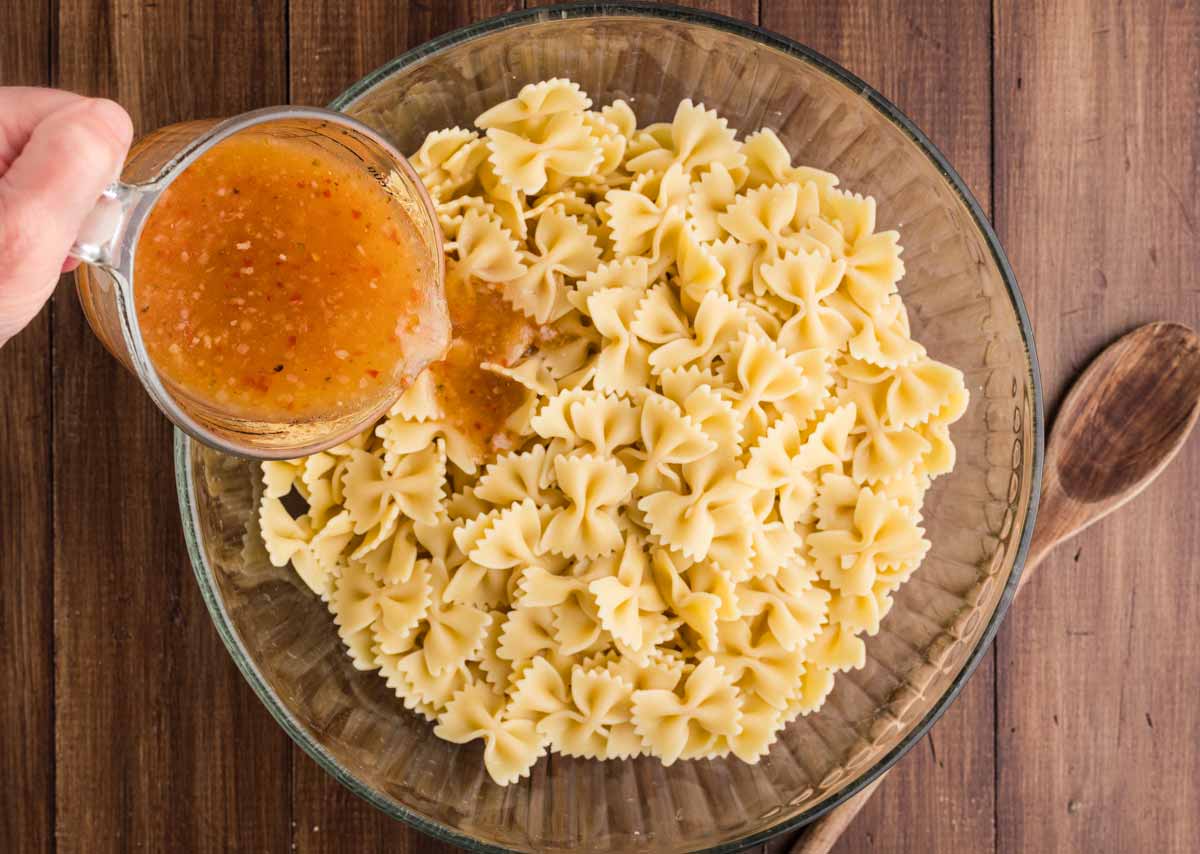 pouring dressing over cooked pasta