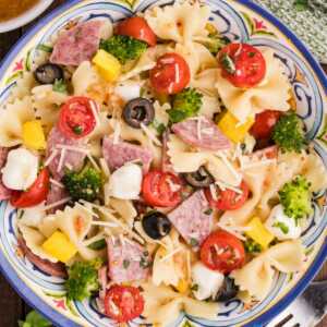 bow tie pasta salad with salami, vegetables, and cheese in colorful bowl