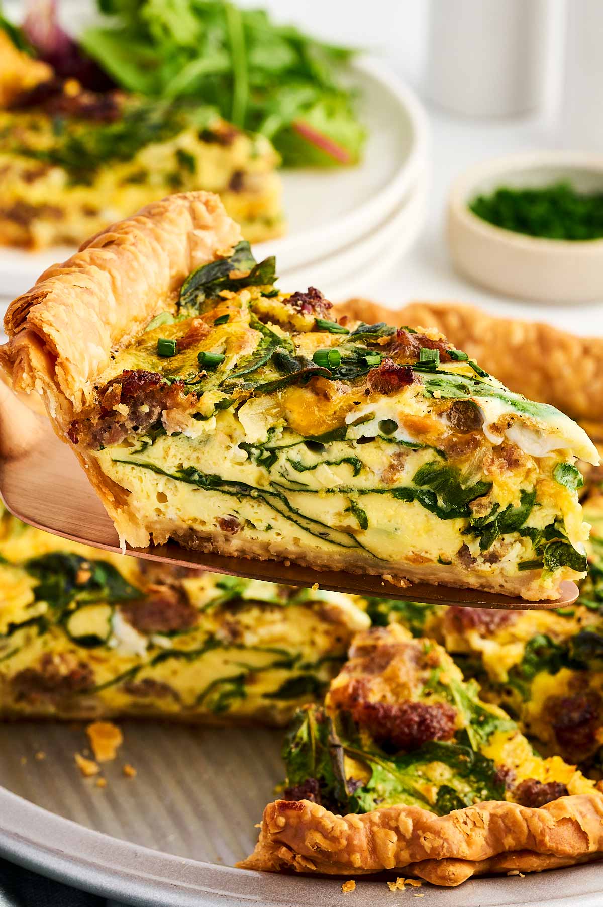 slice of sausage spinach quiche being lifted from pan