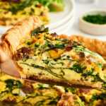 slice of sausage spinach quiche being lifted from pan
