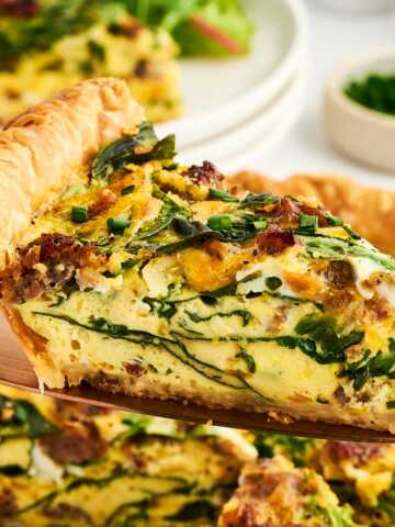 slice of sausage spinach quiche being lifted from pan